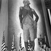 A color guard holding American flags and a banner inscribed with the Nazi swastika stands before an immense portrait of George Washington